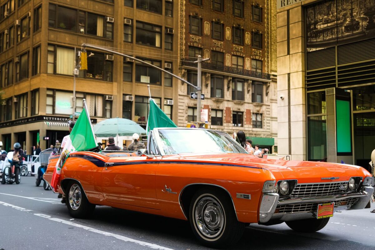 Simva Auto A classic orange convertible with flags during a parade on a New York City street.
