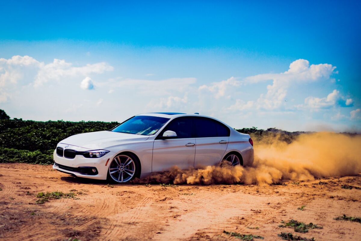 À propos White luxury car drifting on a dirt road, creating a dramatic dust cloud under a blue sky.