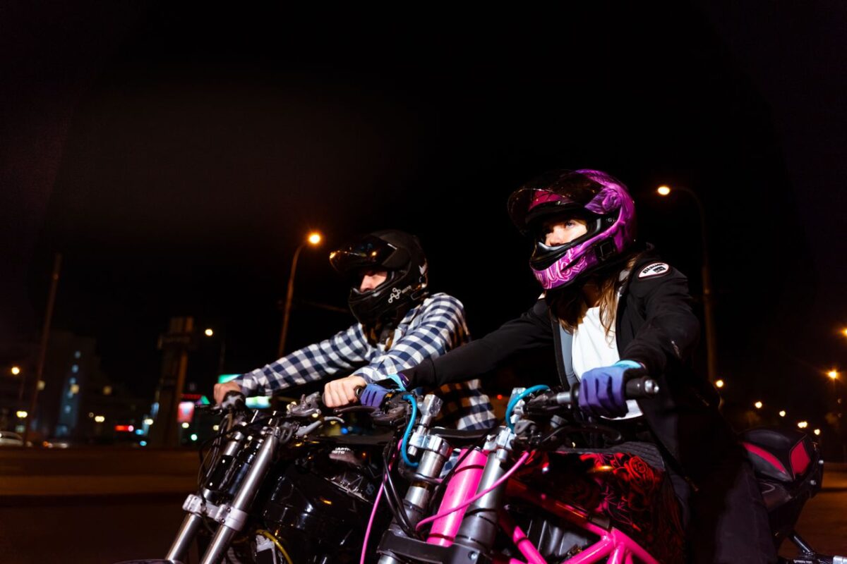 Simva Auto A couple of bikers riding motorcycles at night in urban setting, showcasing vibrant energy.